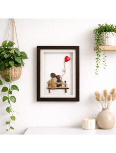 Handmade 3D pebble art depicting a couple on a twig bench with a red heart balloon, framed.